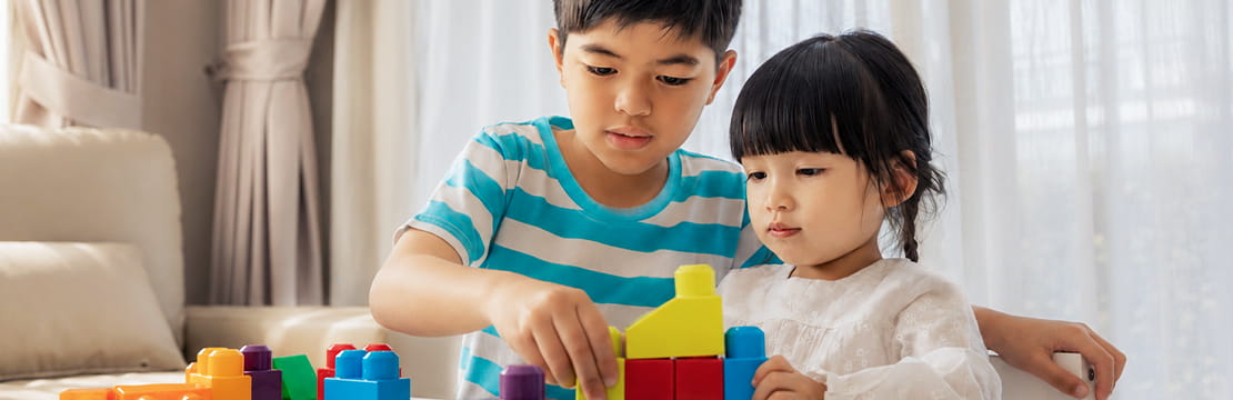 Two siblings work together to build a structure with colorful blocks at a table, illustrating how sibling relationships help form the foundation of family connections and support.